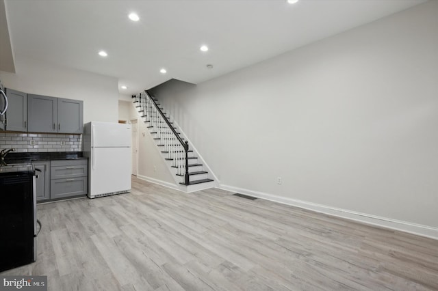 kitchen featuring gray cabinets, light hardwood / wood-style floors, white refrigerator, and backsplash