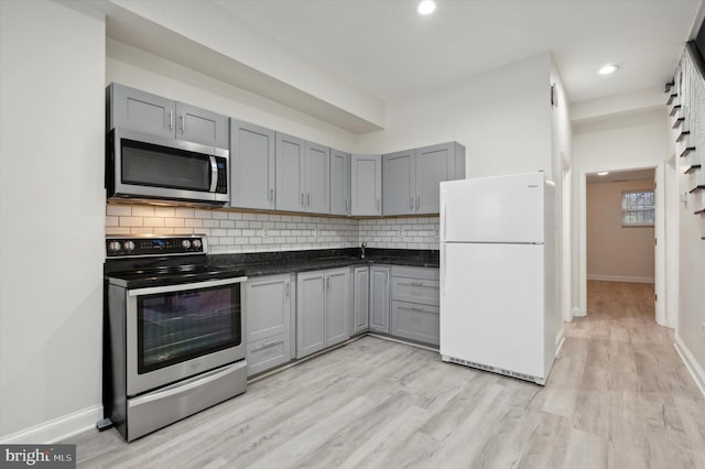 kitchen with appliances with stainless steel finishes, backsplash, light hardwood / wood-style floors, and gray cabinetry