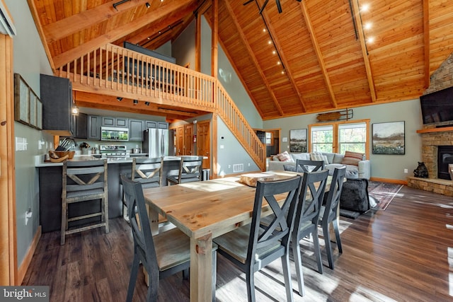 dining room with wood ceiling, a stone fireplace, high vaulted ceiling, rail lighting, and dark hardwood / wood-style floors