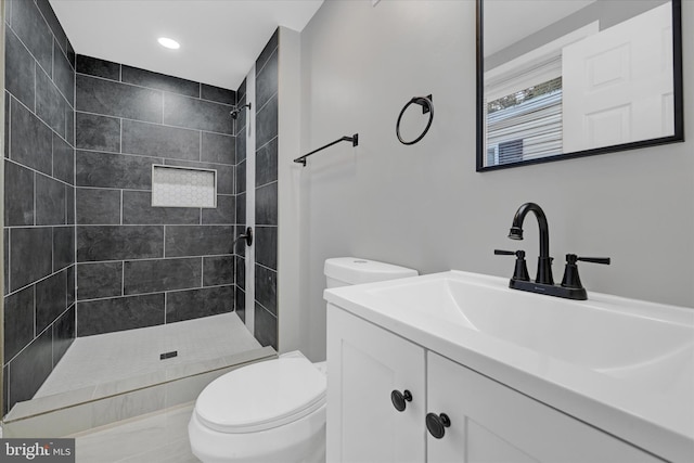 bathroom with a tile shower, vanity, and toilet