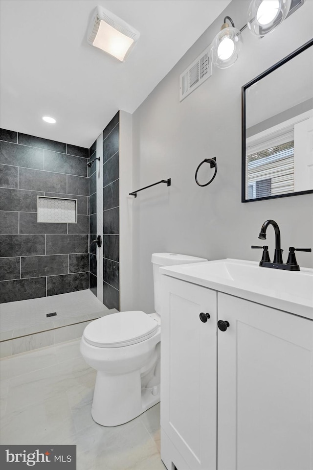 bathroom featuring a tile shower, vanity, and toilet