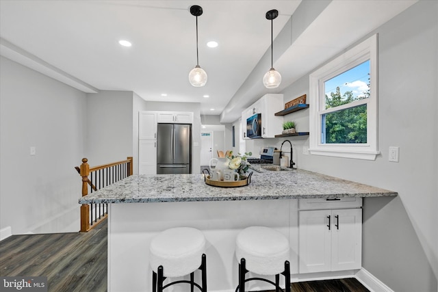 kitchen with stainless steel appliances, white cabinets, kitchen peninsula, and hanging light fixtures