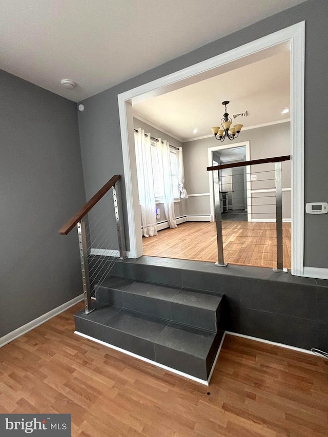 staircase with ornamental molding, a baseboard heating unit, hardwood / wood-style floors, and a notable chandelier