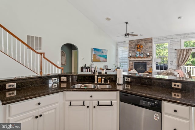 kitchen featuring white cabinets, a fireplace, dark stone countertops, ceiling fan, and stainless steel dishwasher