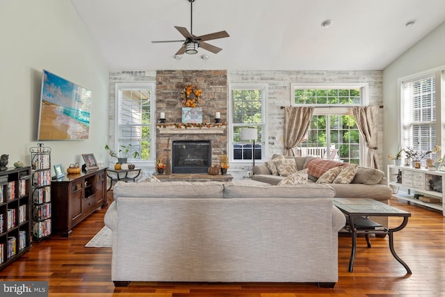 living room with ceiling fan, a stone fireplace, vaulted ceiling, and dark hardwood / wood-style flooring