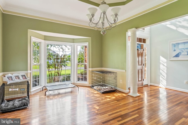 living area with ornamental molding, a notable chandelier, hardwood / wood-style floors, and ornate columns