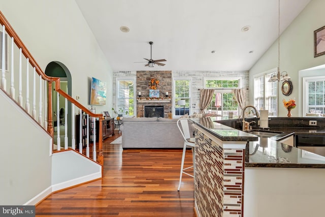 kitchen with a breakfast bar area, ceiling fan with notable chandelier, sink, a fireplace, and dark hardwood / wood-style flooring