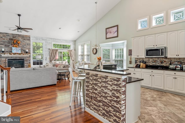 kitchen featuring ceiling fan, a stone fireplace, decorative light fixtures, high vaulted ceiling, and white cabinetry