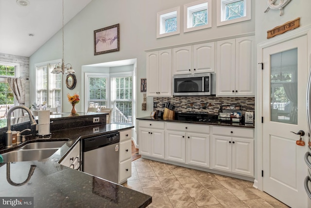 kitchen featuring dark stone countertops, high vaulted ceiling, white cabinets, stainless steel appliances, and sink