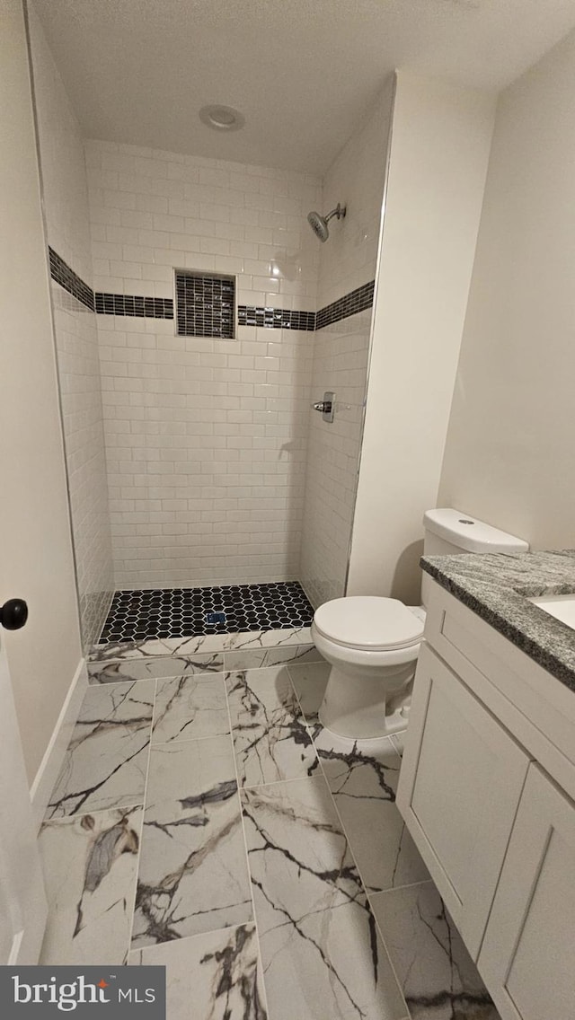 bathroom featuring vanity, a tile shower, and toilet