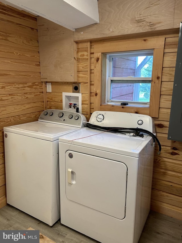 clothes washing area with light hardwood / wood-style flooring, wood walls, and washer and dryer