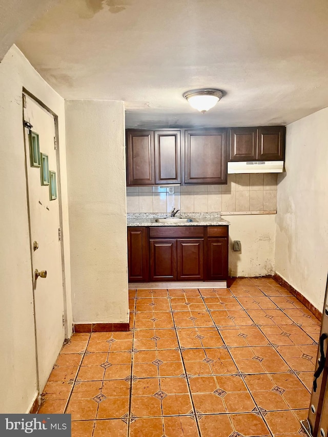 kitchen with dark brown cabinetry, sink, backsplash, and light tile patterned floors