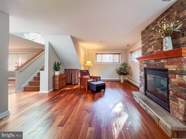 sitting room with a stone fireplace, hardwood / wood-style flooring, a healthy amount of sunlight, and a baseboard heating unit