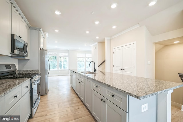 kitchen with light stone counters, sink, a kitchen island with sink, stainless steel appliances, and light wood-type flooring