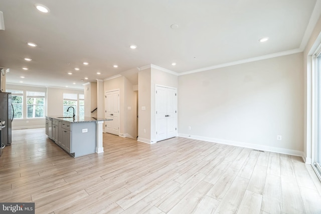 kitchen with a center island with sink, ornamental molding, light stone countertops, and light hardwood / wood-style flooring