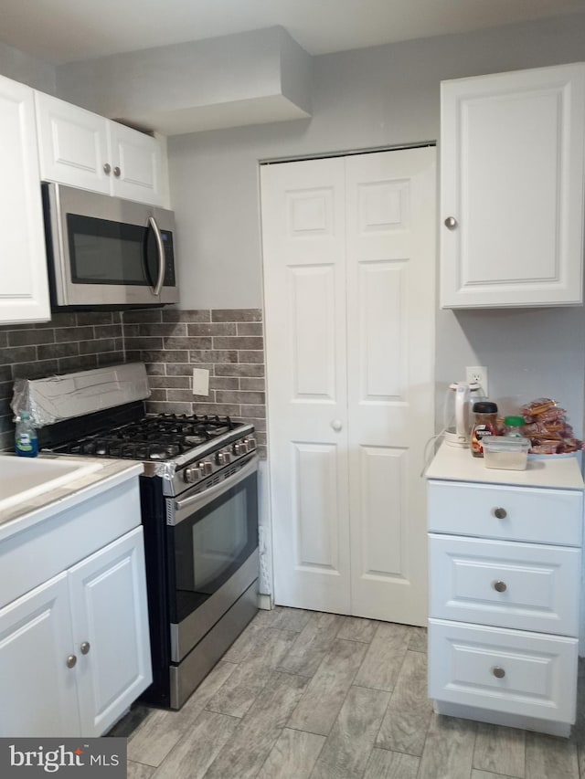 kitchen with stainless steel appliances, light hardwood / wood-style floors, backsplash, and white cabinetry