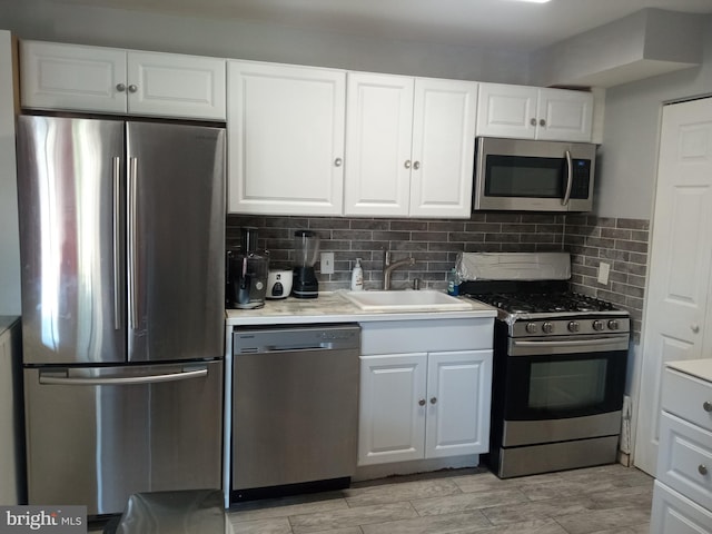 kitchen with appliances with stainless steel finishes, white cabinetry, sink, and backsplash