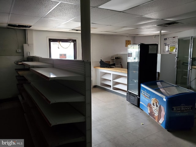 basement with a drop ceiling and black fridge