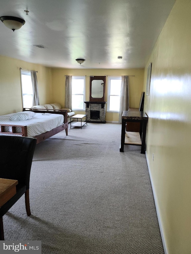 bedroom featuring light colored carpet and a stone fireplace