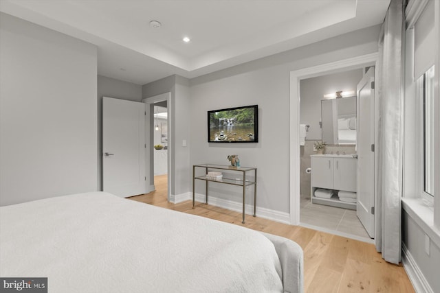 bedroom featuring light wood-type flooring, ensuite bath, and a tray ceiling