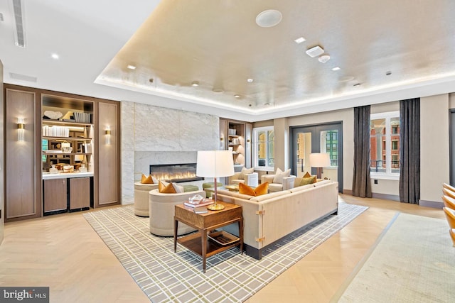 living room with a fireplace, a raised ceiling, and light parquet floors