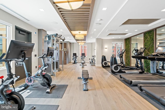 gym featuring light wood-type flooring and a tray ceiling