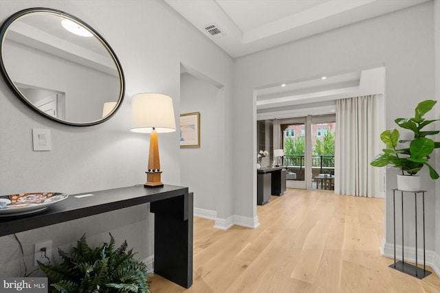 hallway with light wood-type flooring and a raised ceiling