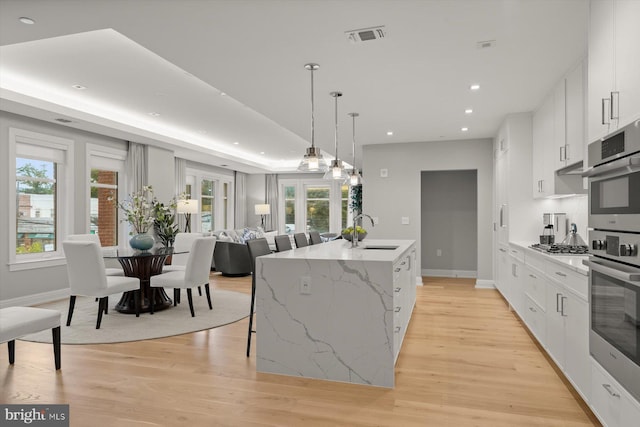 kitchen featuring white cabinetry, light wood-type flooring, oven, a center island with sink, and sink