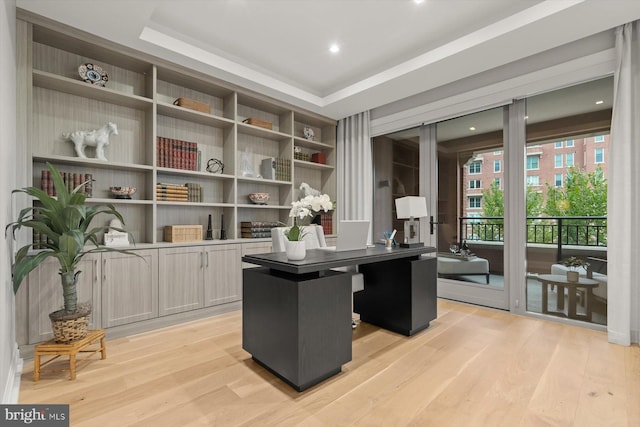 office area with light hardwood / wood-style floors and a tray ceiling