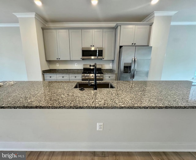 kitchen featuring stone countertops, stainless steel appliances, wood-type flooring, crown molding, and sink