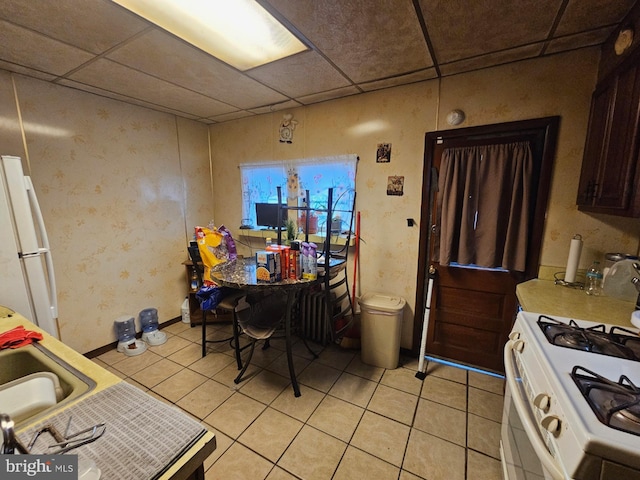 kitchen with dark brown cabinets, a paneled ceiling, light tile patterned floors, and white appliances