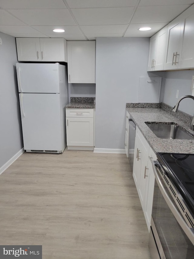 kitchen with baseboards, white cabinets, a sink, light stone countertops, and stainless steel appliances