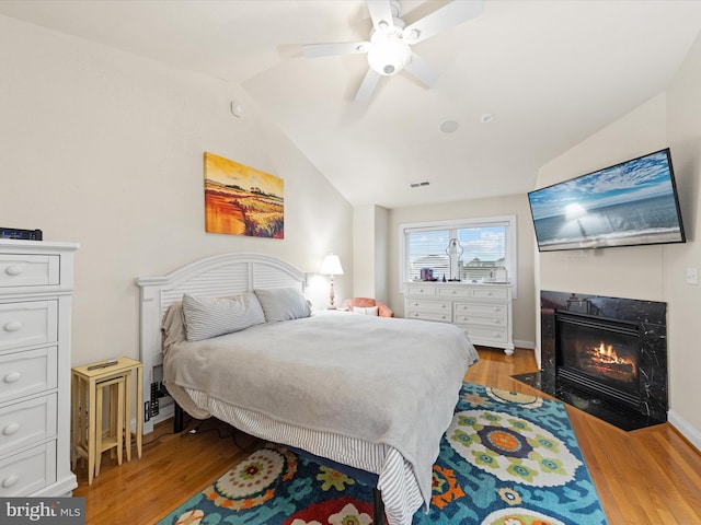 bedroom with ceiling fan, lofted ceiling, light hardwood / wood-style floors, and a high end fireplace