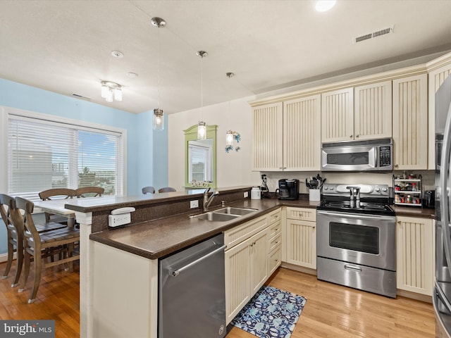 kitchen featuring sink, kitchen peninsula, cream cabinets, appliances with stainless steel finishes, and light hardwood / wood-style floors