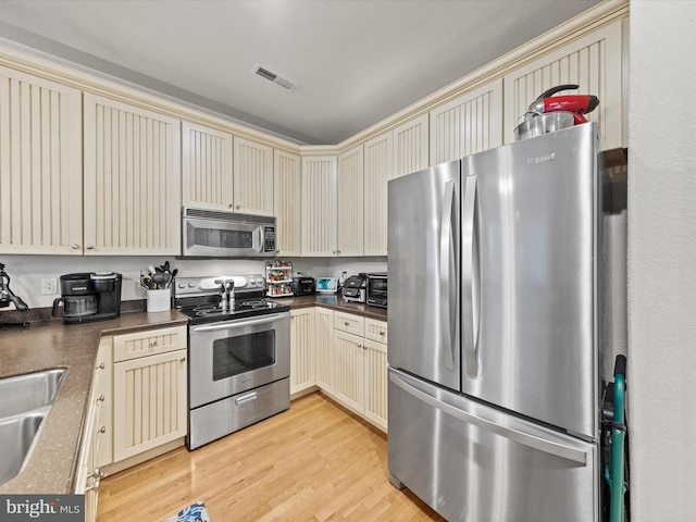 kitchen with light wood-type flooring, stainless steel appliances, and cream cabinetry