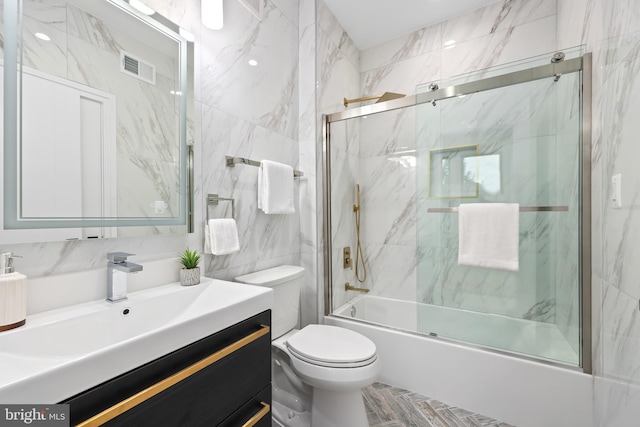 full bathroom with tile walls, vanity, toilet, and bath / shower combo with glass door