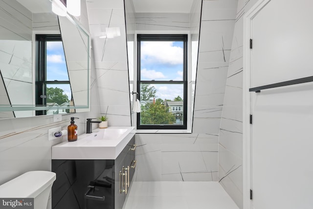 bathroom featuring a healthy amount of sunlight, tile walls, vanity, and toilet