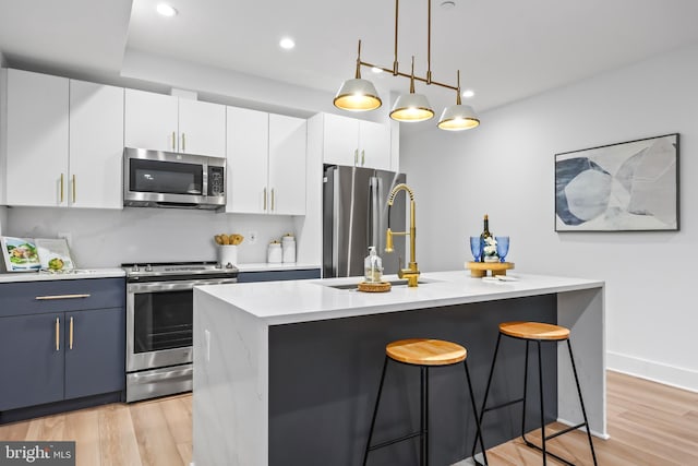 kitchen with pendant lighting, an island with sink, white cabinetry, stainless steel appliances, and light wood-type flooring