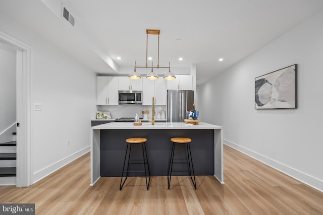 kitchen featuring pendant lighting, white cabinets, appliances with stainless steel finishes, and a kitchen island with sink