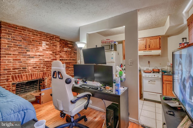 office area featuring light hardwood / wood-style flooring, a textured ceiling, brick wall, and a fireplace