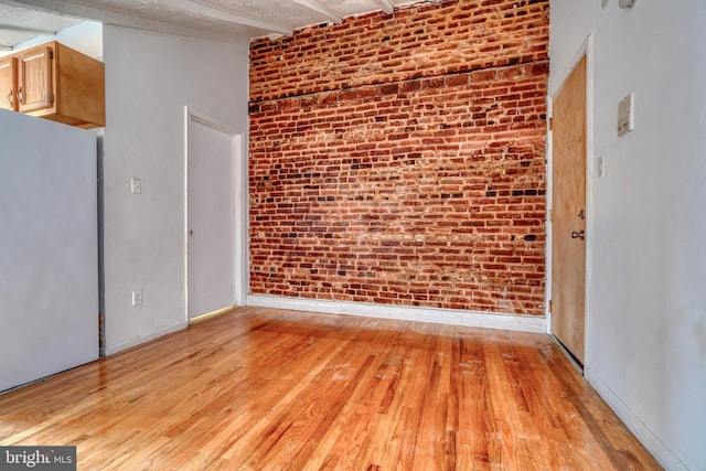 spare room with brick wall and light hardwood / wood-style flooring