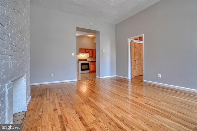 unfurnished living room with a textured ceiling, light hardwood / wood-style floors, and a brick fireplace