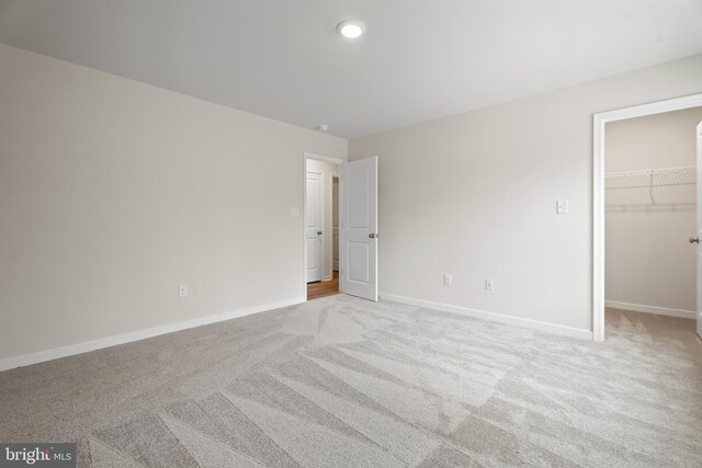 unfurnished bedroom with a spacious closet, a closet, light carpet, and baseboards
