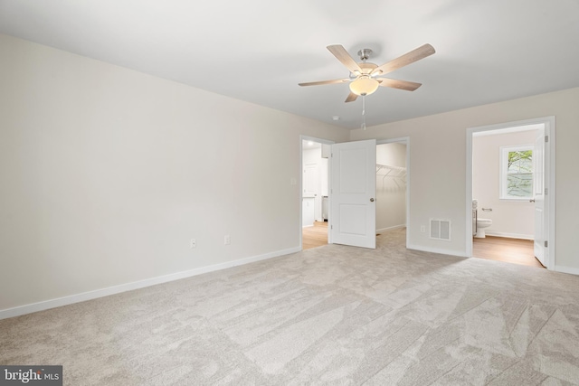 unfurnished bedroom featuring light colored carpet, visible vents, baseboards, and a walk in closet