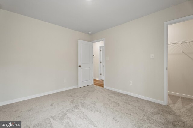 unfurnished bedroom featuring a closet, a walk in closet, carpet, and baseboards
