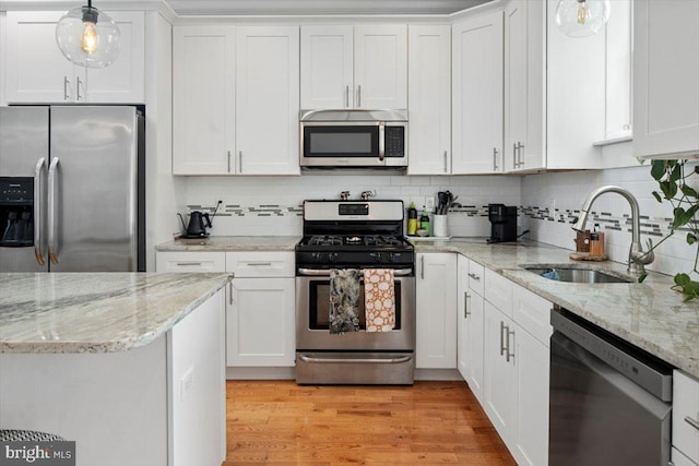 kitchen featuring white cabinets, decorative light fixtures, appliances with stainless steel finishes, and light hardwood / wood-style flooring