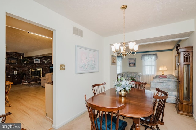 dining room with a textured ceiling, a chandelier, light hardwood / wood-style flooring, and a brick fireplace