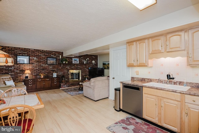 kitchen featuring light brown cabinets, sink, stainless steel dishwasher, brick wall, and light hardwood / wood-style floors