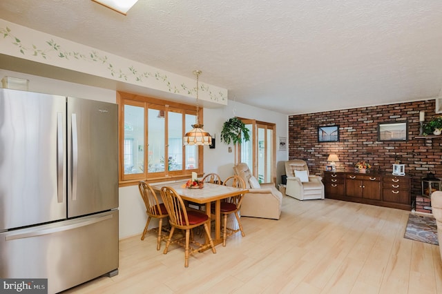 dining area featuring light wood-type flooring, a textured ceiling, and brick wall