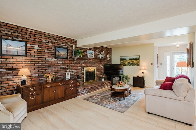 living room featuring brick wall, a textured ceiling, a fireplace, and light hardwood / wood-style floors